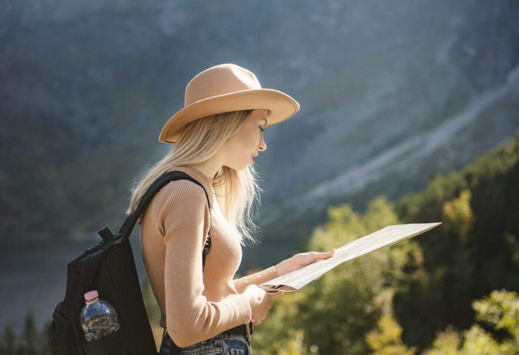 wanderlust and travel concept stylish traveler girl in hat looking at map exploring woods e1712714886988